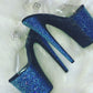 Platform heels with clear straps, and dual Ombre with blue and black glitter. Shades of blue starting at the front of the platform, and back of the heels, blending to black under the arch, and down the inside of the heels. Black soles.