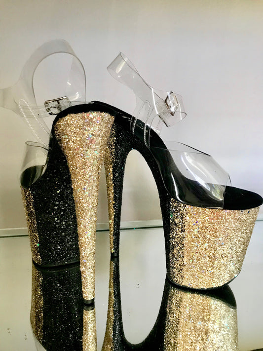 Platform heels with clear straps, and dual Ombre with gold and black glitter. Shades of gold starting at the front of the platform, and back of the heels, blending to black glitter under the arch, and down the inside of the heels. Black soles.