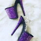 Platform heels with clear straps, and dual Ombre with purple and black glitter. Shade of purple starting at the front of the platform, and back of the heels, blending to black under the arch, and down the inside of the heels. Black soles.  Edit alt text